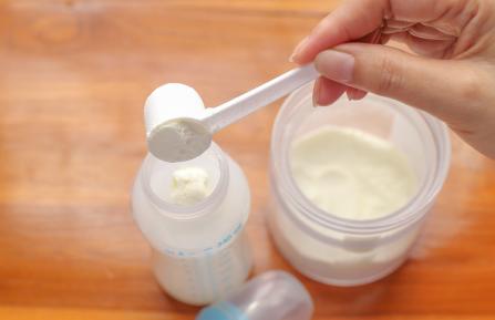 Image of person's hand preparing a bottle of baby formula