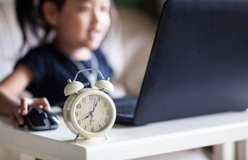 Asian girl working on computer with alarm clock in foreground