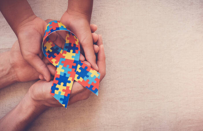 Image of adult and child hands hold a puzzle-piece printed autism ribbon